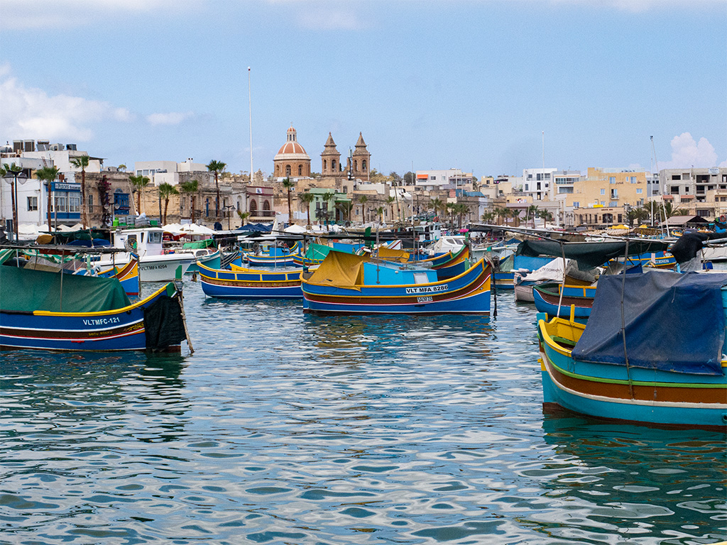 Port rybacki, kolorowe łodzie przykryte plandekami, w tle miasteczko, domy i wieże koscioła